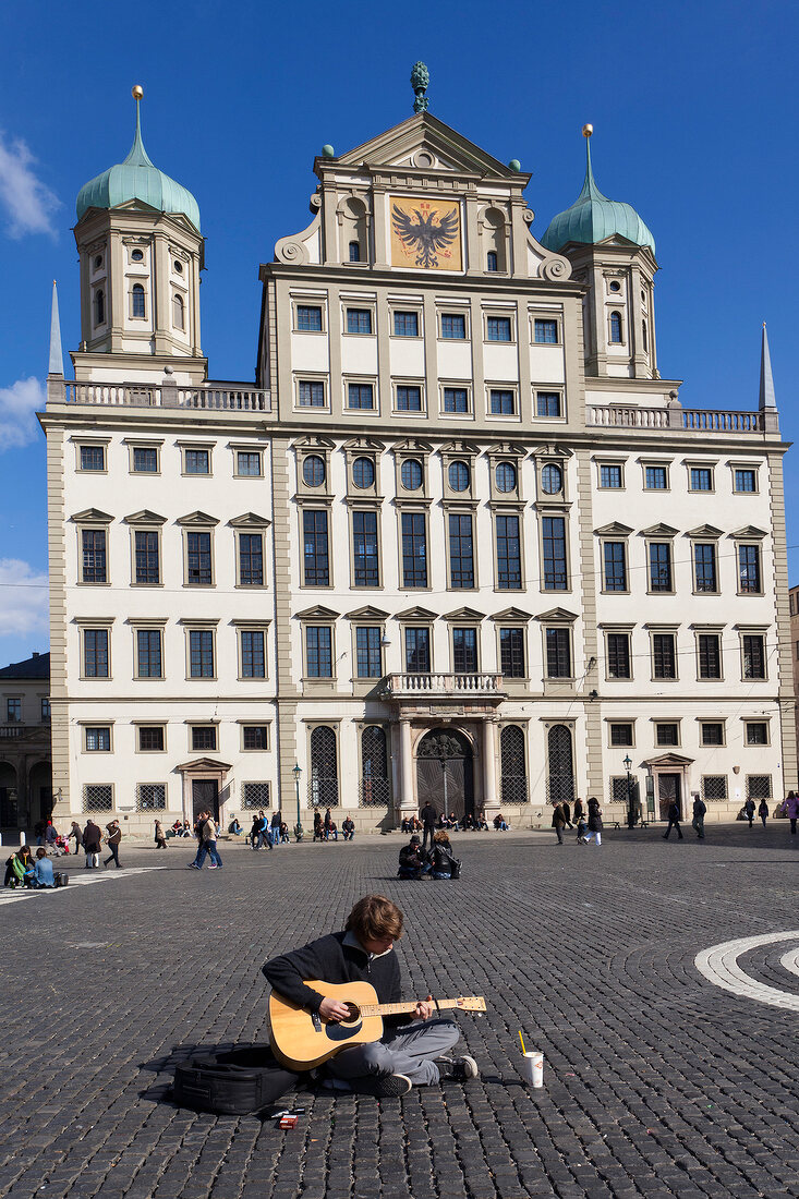 Man playing guitar in front of Augsburg Town Hall in Augsburg, Bavaria, Germany