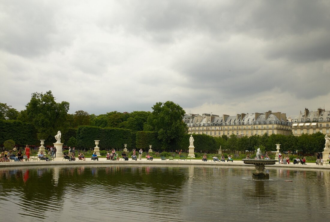 Tourists relaxing near water in Tuileries Garden in front of Roue de Paris, Paris, France