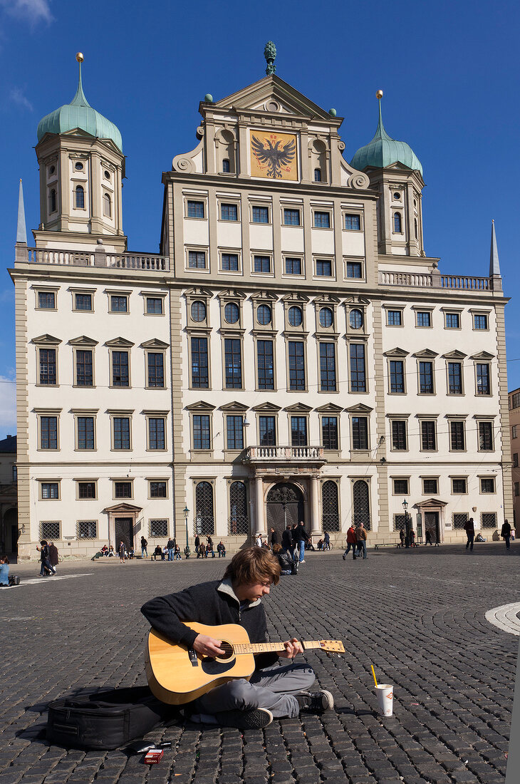Man playing guitar in front of Augsburg Town Hall in Augsburg, Bavaria, Germany