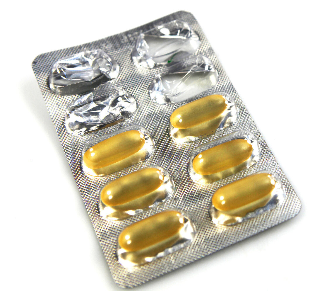 Close-up of six yellow capsules in pack on white background, cut out