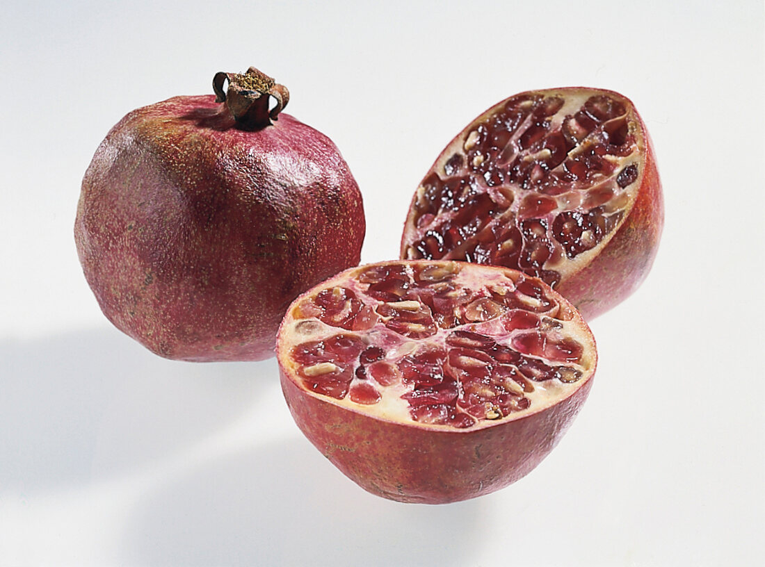 Whole and halves of pomegranates on white background