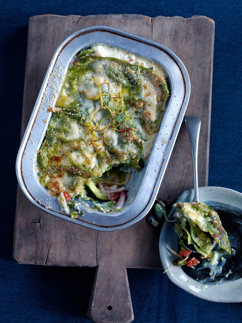 Green lasagne with zucchini in baking dish on wooden platter