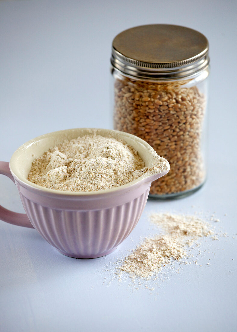 Whole wheat flour in cup and lentils in glass jar