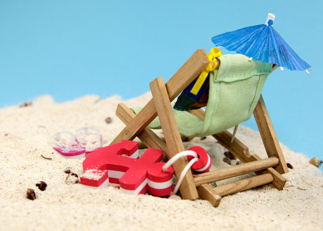 View of deck chair, anchor, sunshade and flip flops on sand