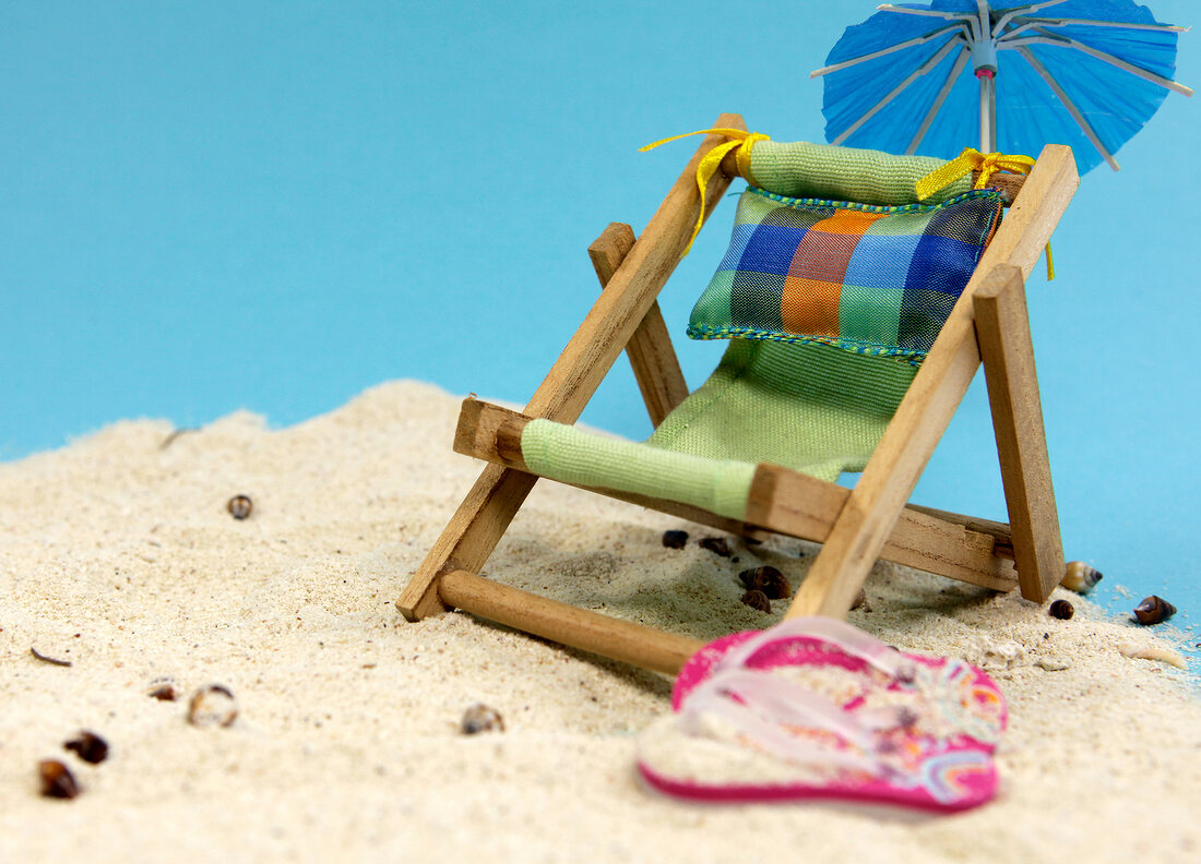 Beach chair with flip flops and umbrella on sand