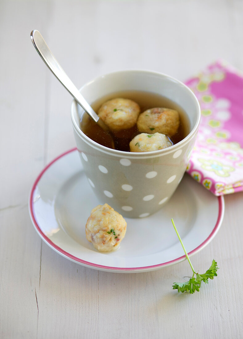 Cup of beef bouillon with dumplings on saucer