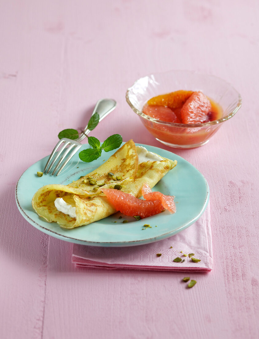 Pancakes with citrus fruit on plate with bowl of citrus fruits