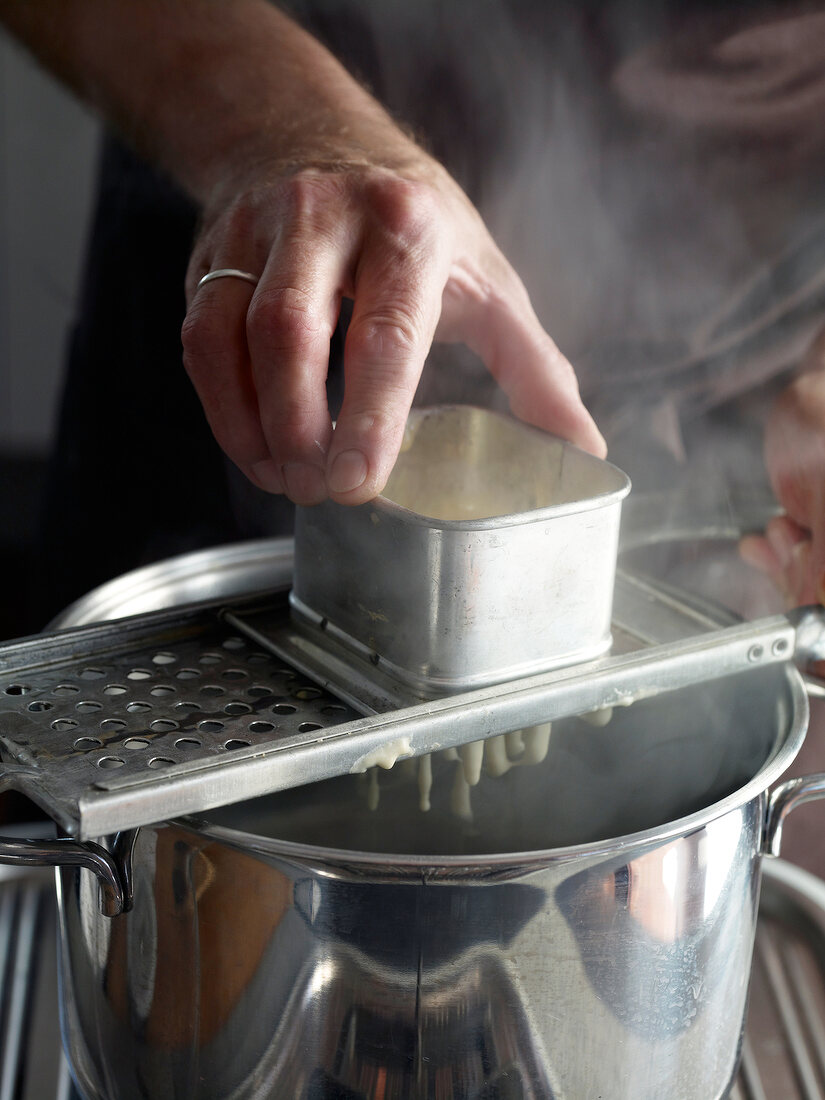 Close-up of dough passing through spaetzle maker while preparing spaetzle, step 3