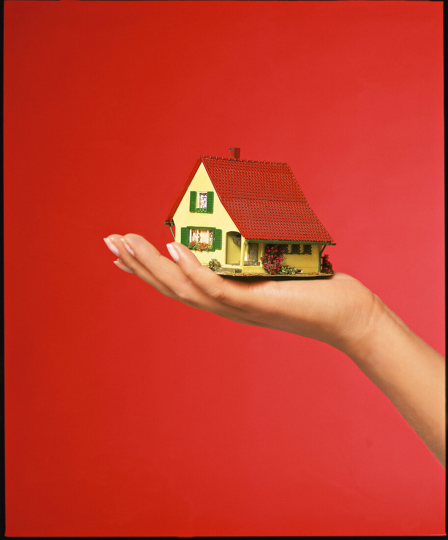 Close-up of person holding small artificial house against red background