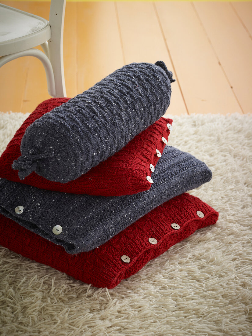 Stack of cushion with knitted cover on white fur carpet