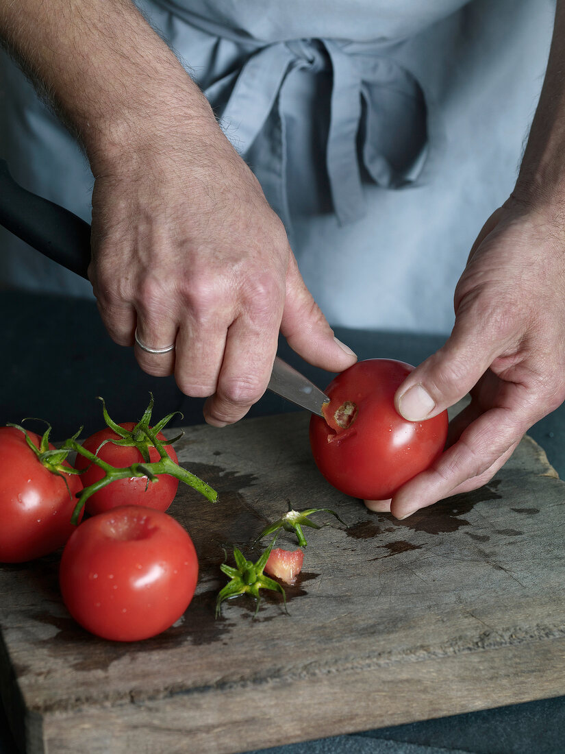 Close-up of stem of tomato being cut for preparation of tomato sauce, step 1