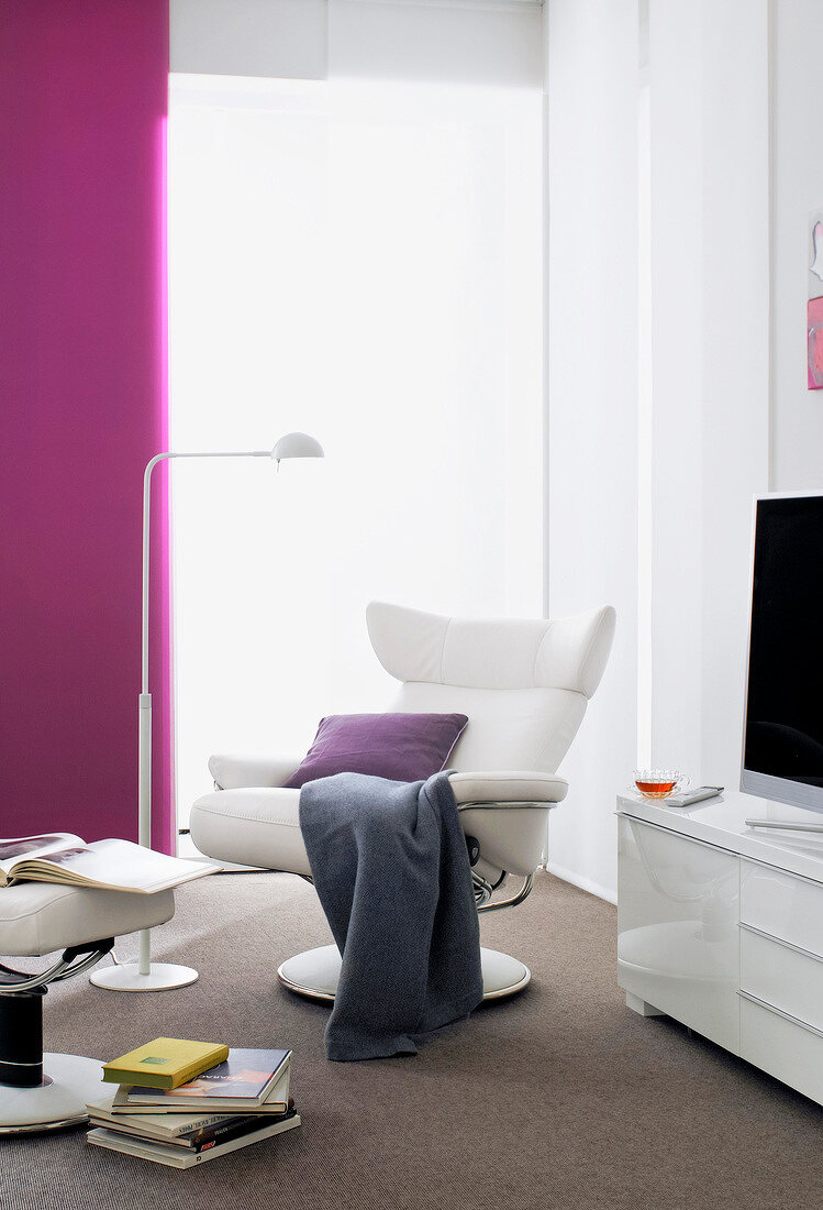 Armchair, floor lamp and magazines on stool in living room