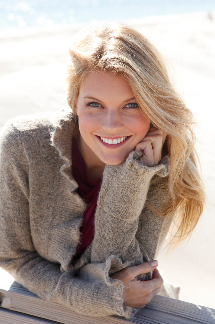 Portrait of beautiful blonde woman wearing brown knitted jacket with head propped on hand