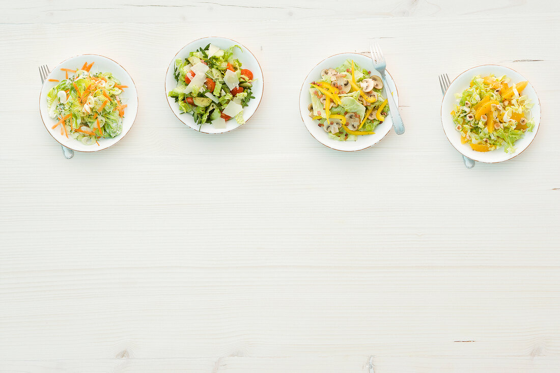 Four different salads on plates, overhead view