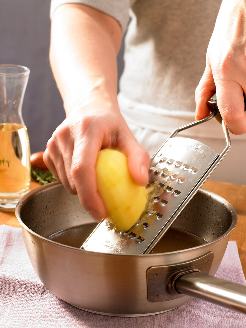 Close-up of hand grating potato in pan