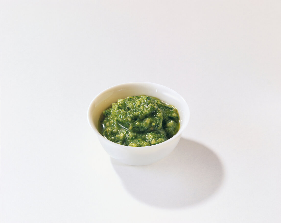 Green pesto in bowl on white background