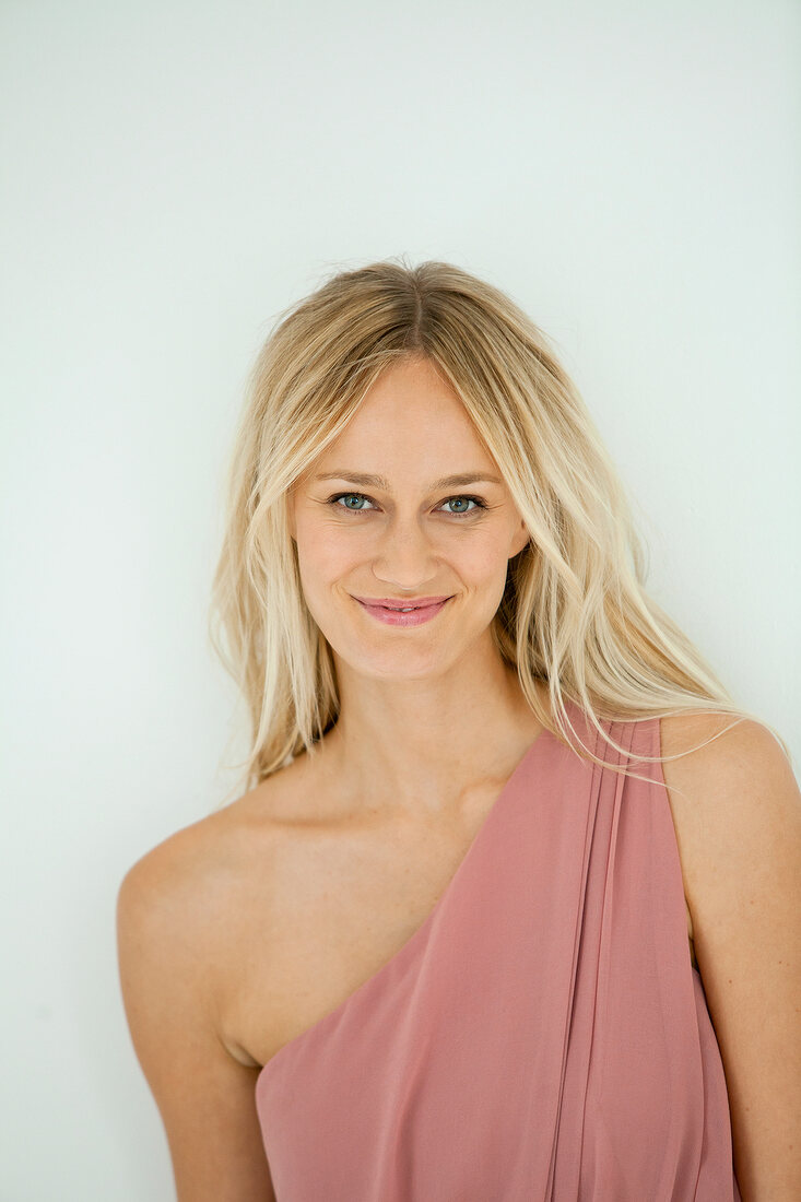 Portrait of gray eyed beautiful woman with blonde hair wearing pink dress, smiling 