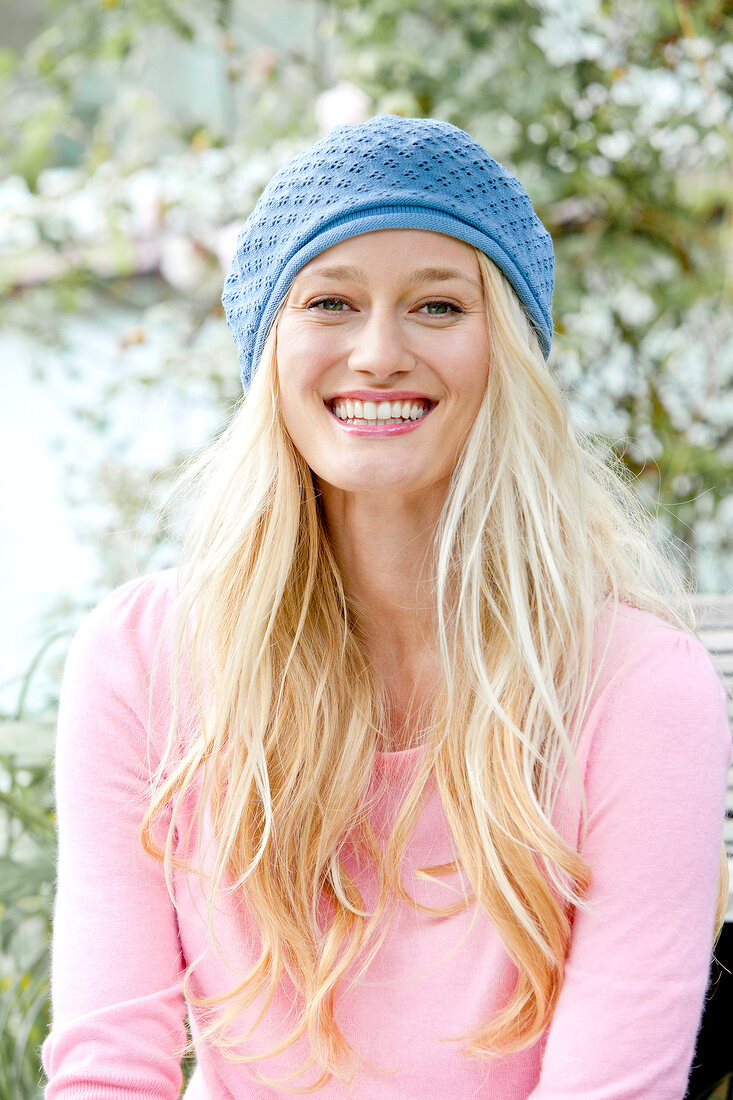 Portrait of happy blonde woman with long hair wearing pink top and blue cap, smiling
