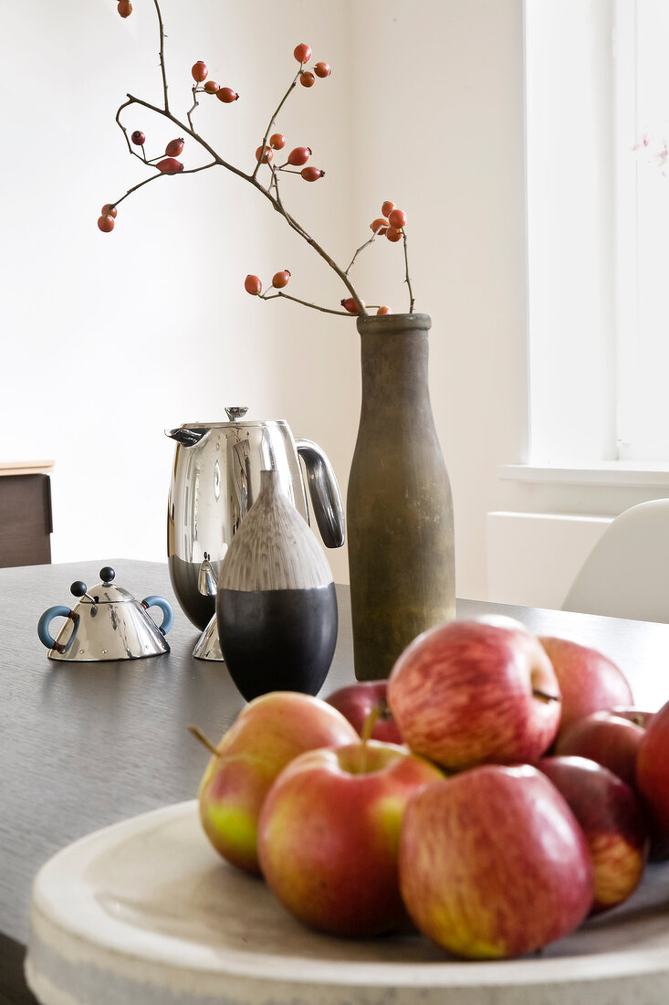 Close-up of bowl of apples with rose hip branch and teapot on table