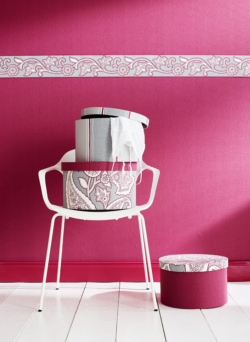 Hutschachteln auf weißem Stuhl, vor pinkfarbener Wand