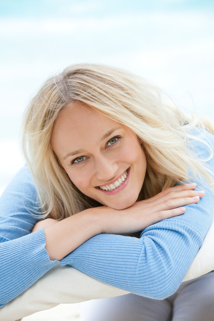 Portrait of happy blonde woman wearing blue sweater smiling and relaxing on beach
