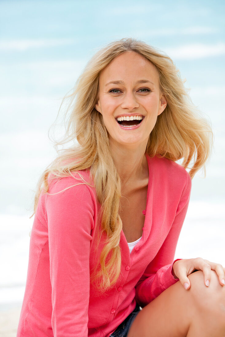 Portrait of happy blonde woman wearing pink sweater laughing with hand on her knee