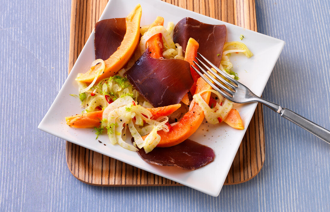 Dried meat salad with fennel and raw papaya on square plate
