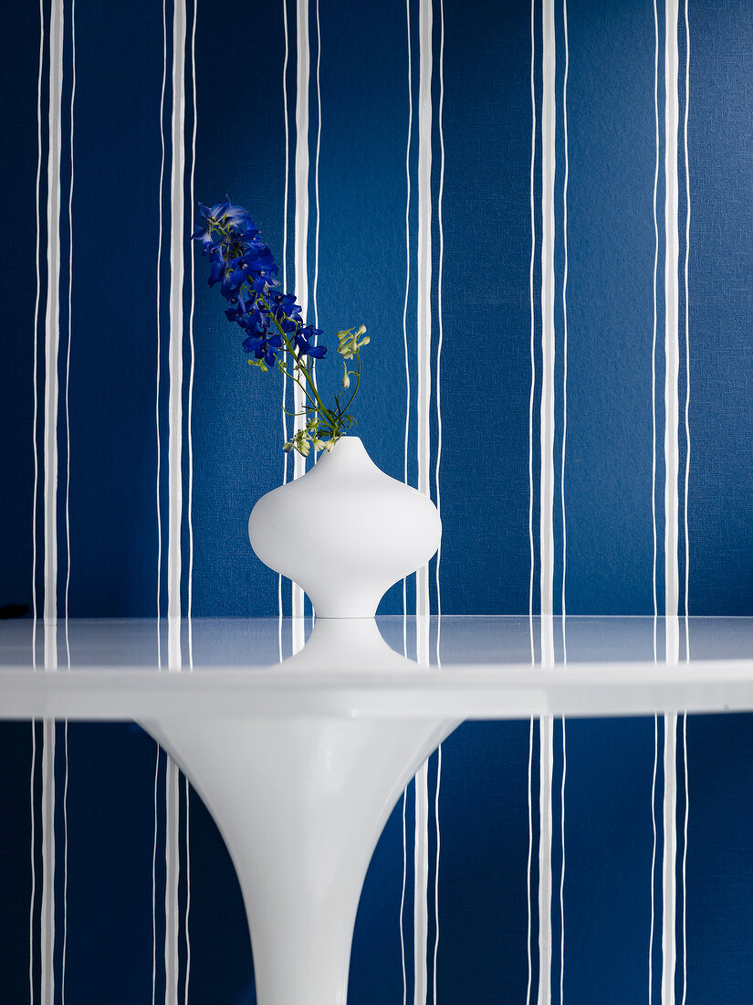 Close-up of white vase on white table against blue striped background