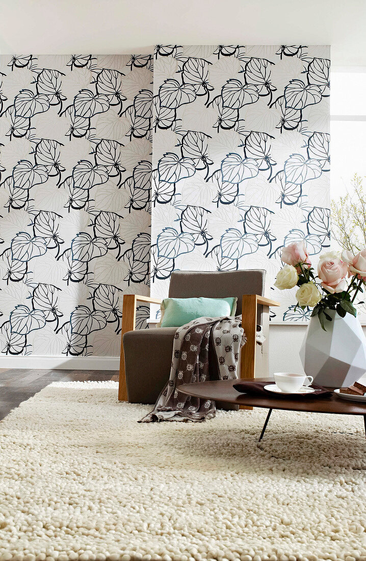 Living room with armchair, table and large leaves patterned wallpaper