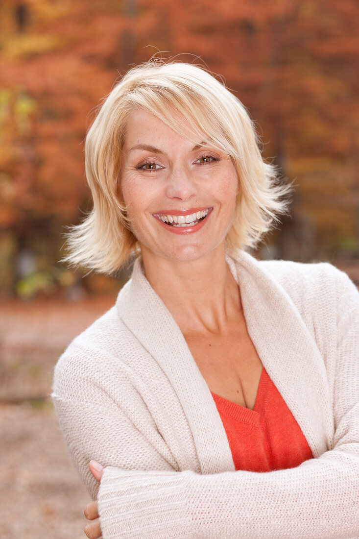 Portrait of happy blonde woman with short hair in white sweater, smiling with arms crossed