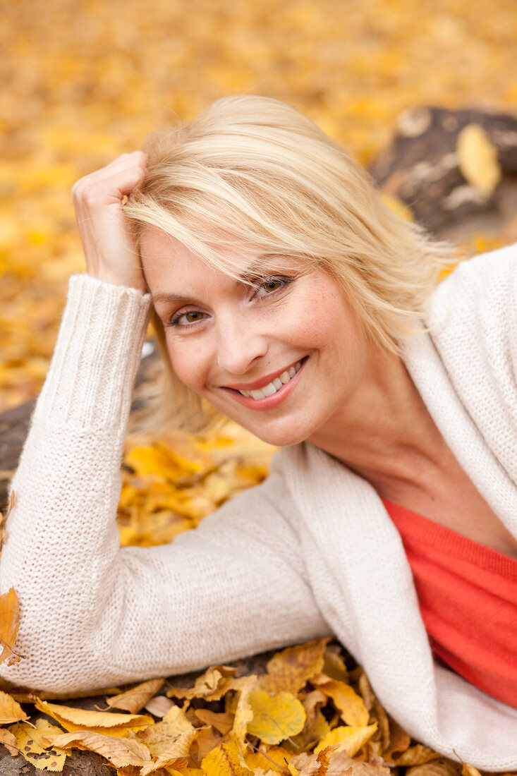 Pretty blonde woman wearing white sweater lying on autumn leaves