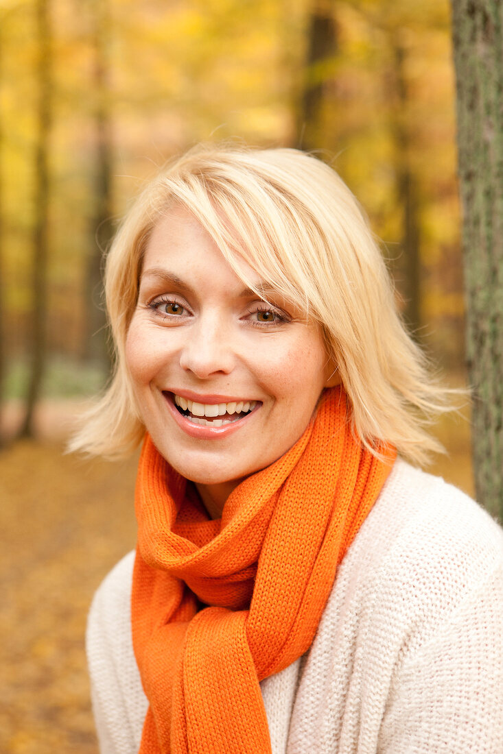 Portrait of happy blonde woman with short hair wearing sweater and orange scarf, smiling
