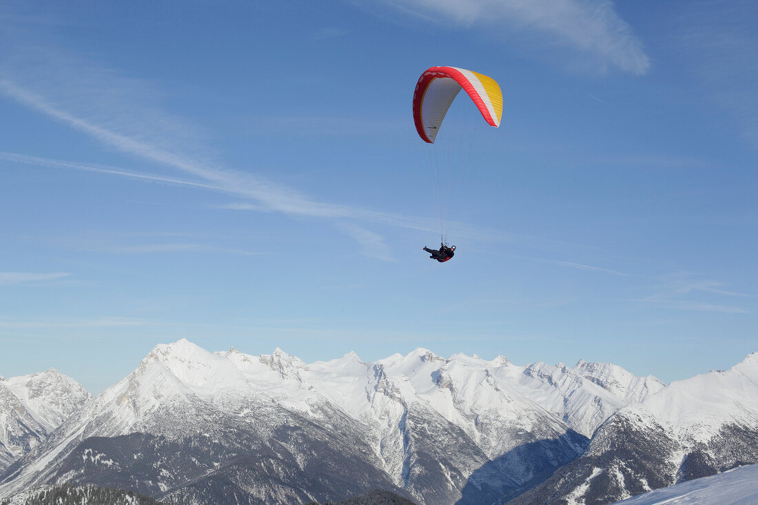 Man paragliding between snow mountains at Leutaschtal, North Tyrol, Italy