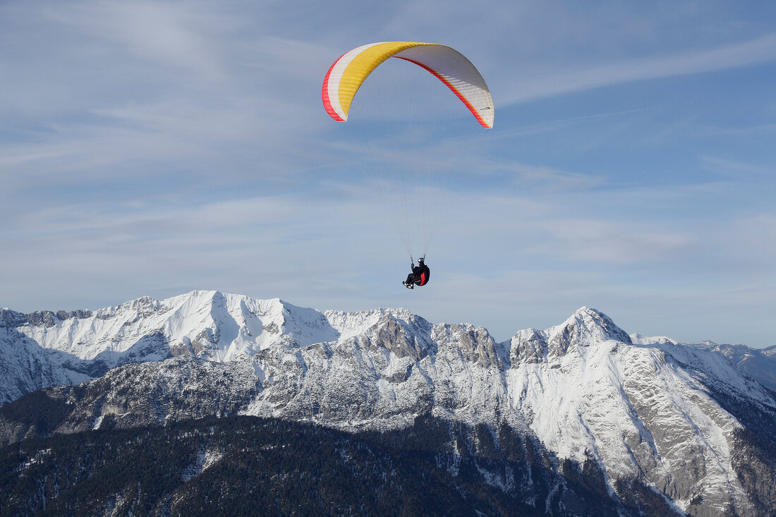 Man paragliding between snow mountains at Leutaschtal, North Tyrol, Italy