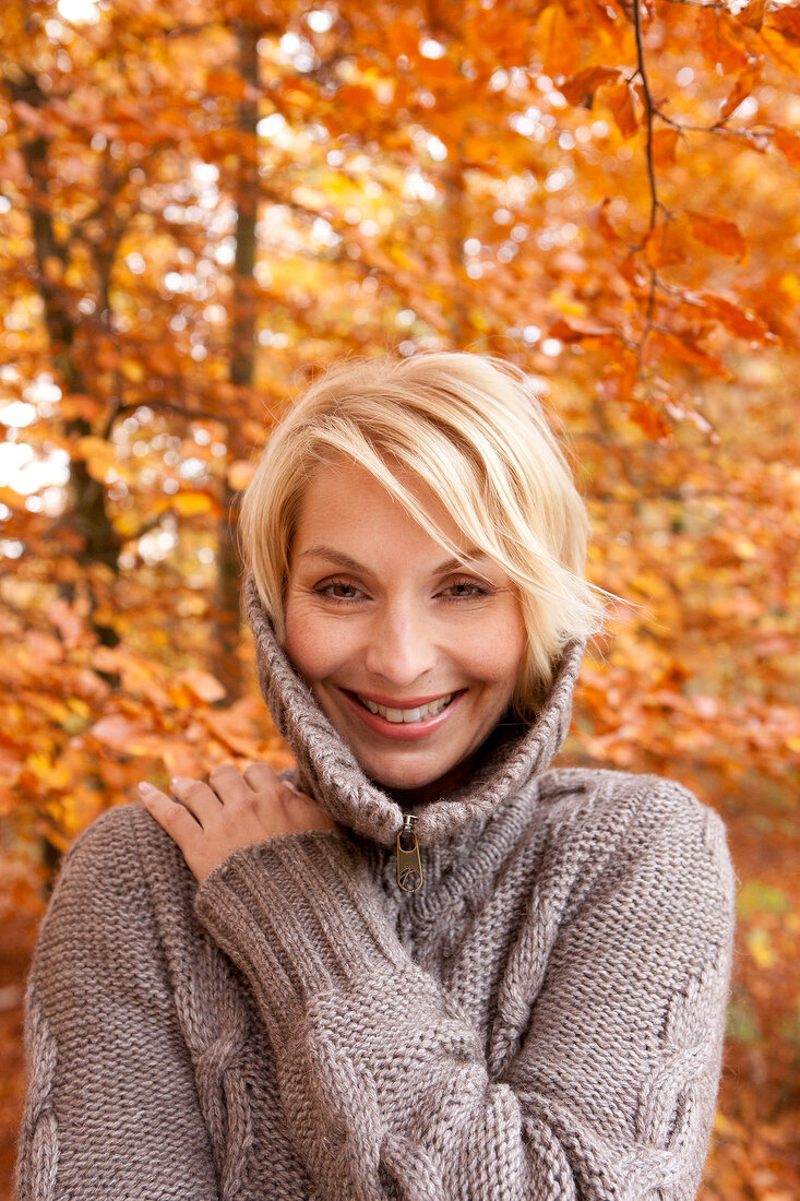 Portrait of pretty blonde woman in gray sweater, smiling with hand on shoulder 