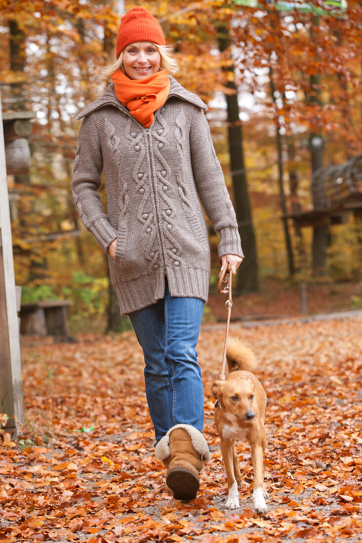 Woman wearing gray cardigan and orange scarf walking with dog in autumn forest