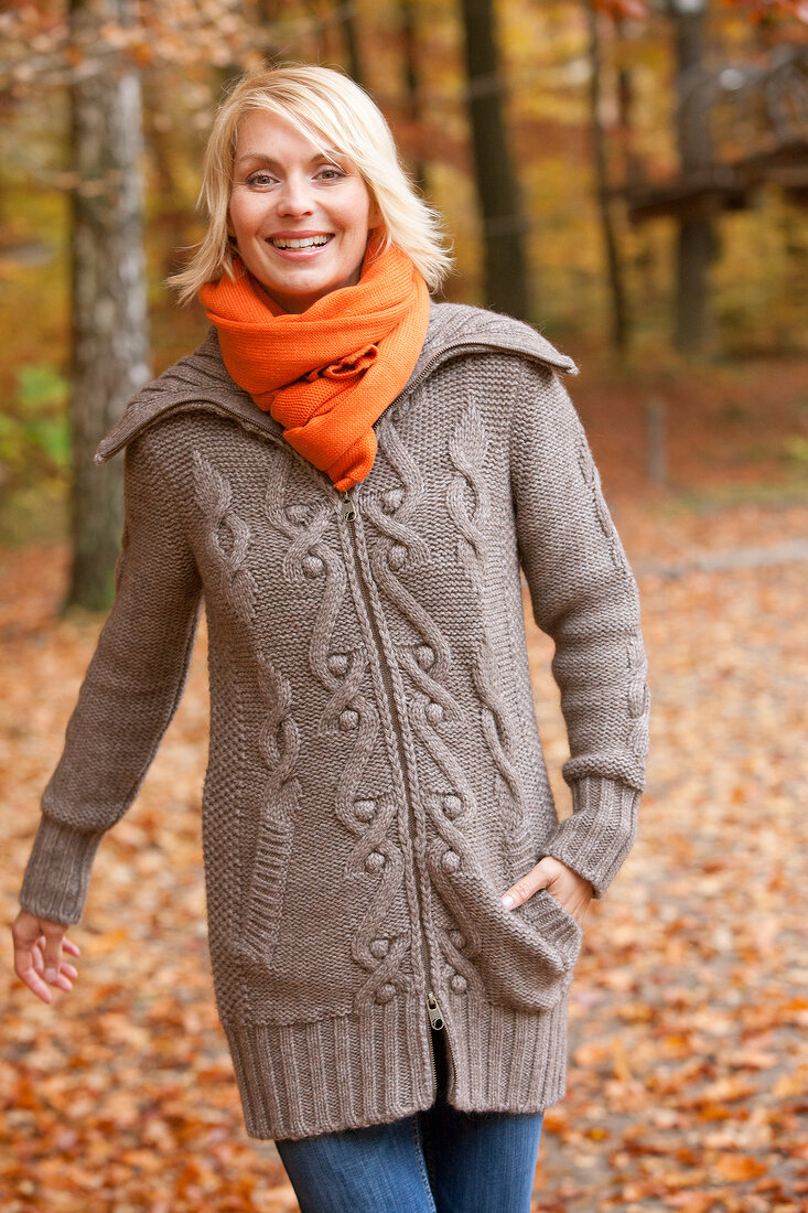 Pretty blonde woman wearing gray sweater and orange scarf smiling in autumn forest