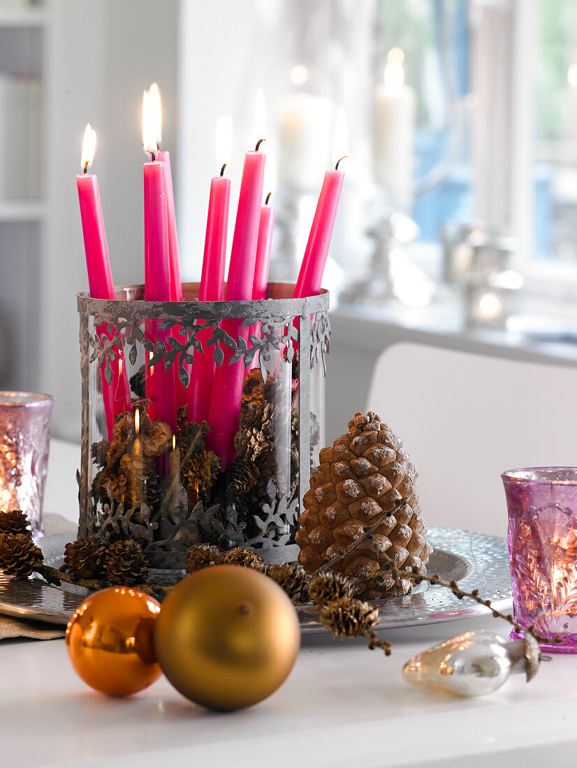 Lit candles in candle holder with larch cones on plate for Christmas