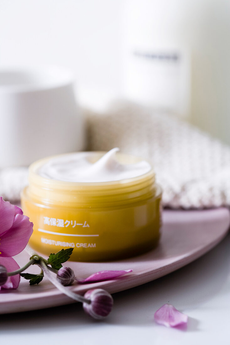 Close-up of flowers and moisturizing cream in container on plate