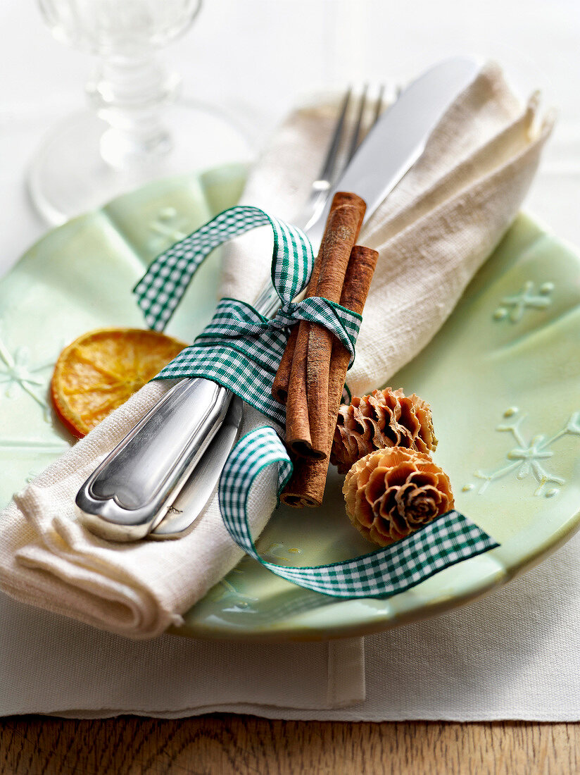 Napkin rolled with cutlery and cinnamon sticks on plate for winter