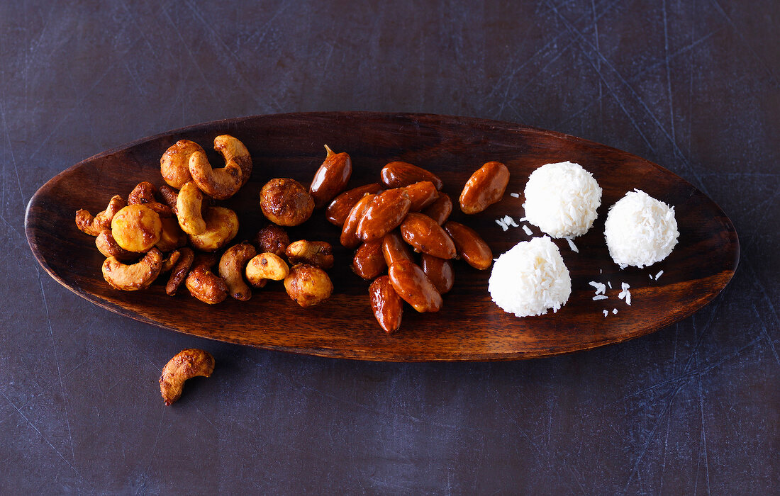 Mixed nuts, roasted almonds and coconut chocolates on wooden platter