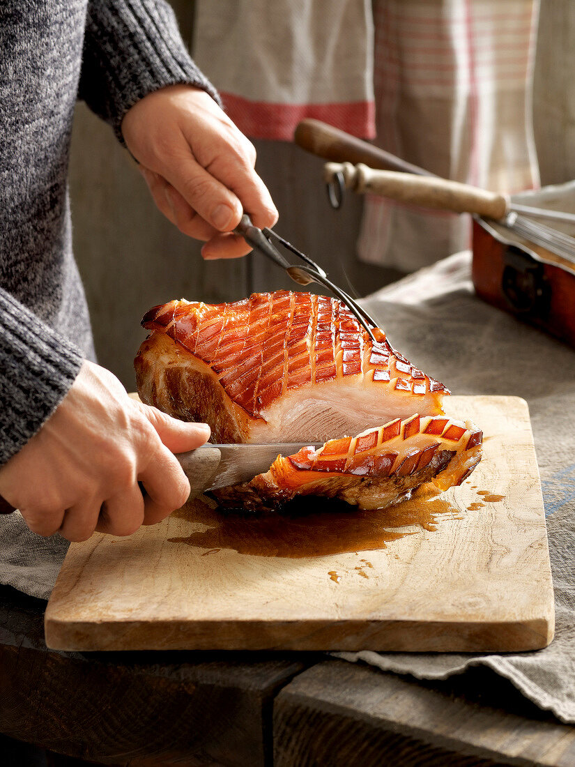 Woman slicing roasted pork with beer sauce on chopping board for winter