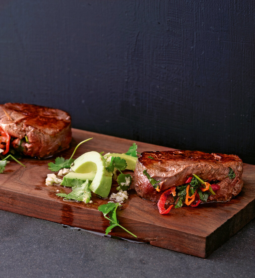 Close-up of spicy beef fillets with avocado on wooden platter