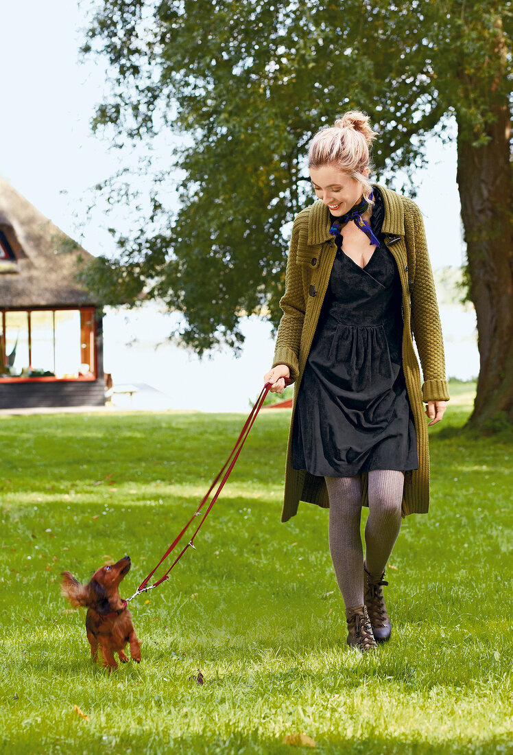 Beautiful blonde woman wearing long coat walking with dachshund dog in park