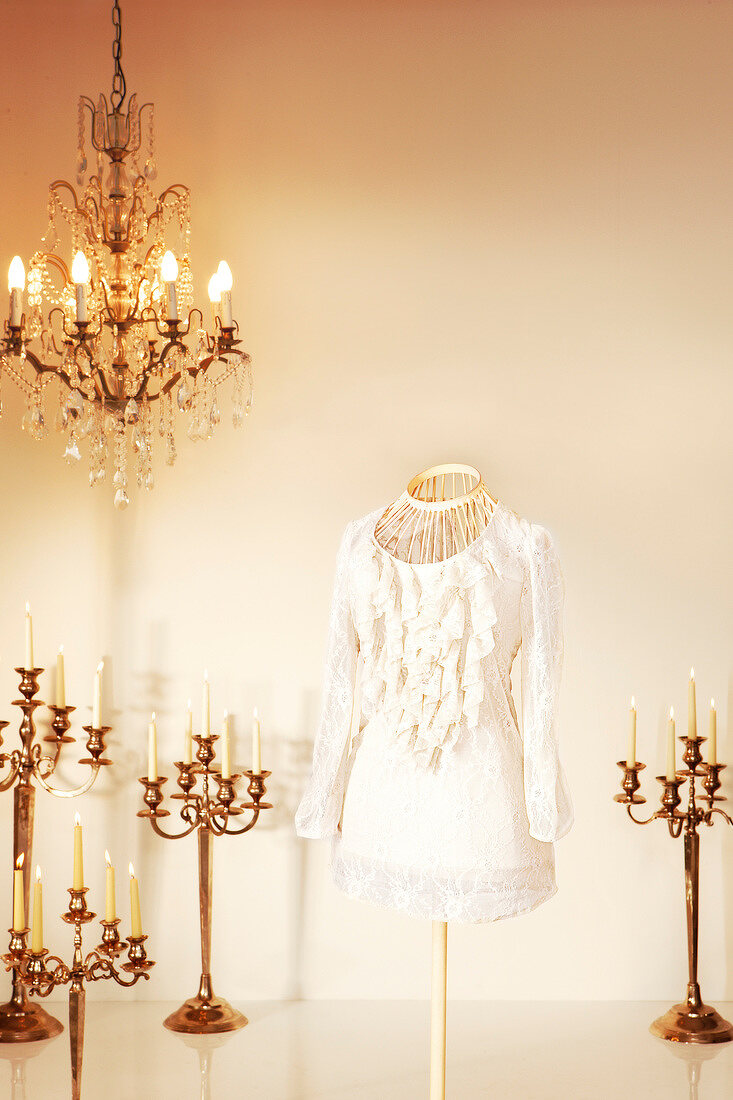 White ruffled blouse on mannequin with chandelier and candlestick around