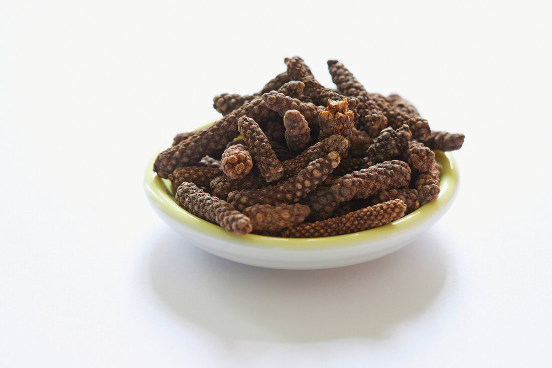 Bowl of long peppercorns on white background