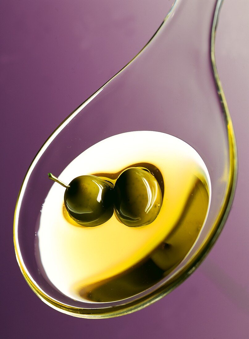 Olivenöl auf Plastiklöffel; grüne Oliven