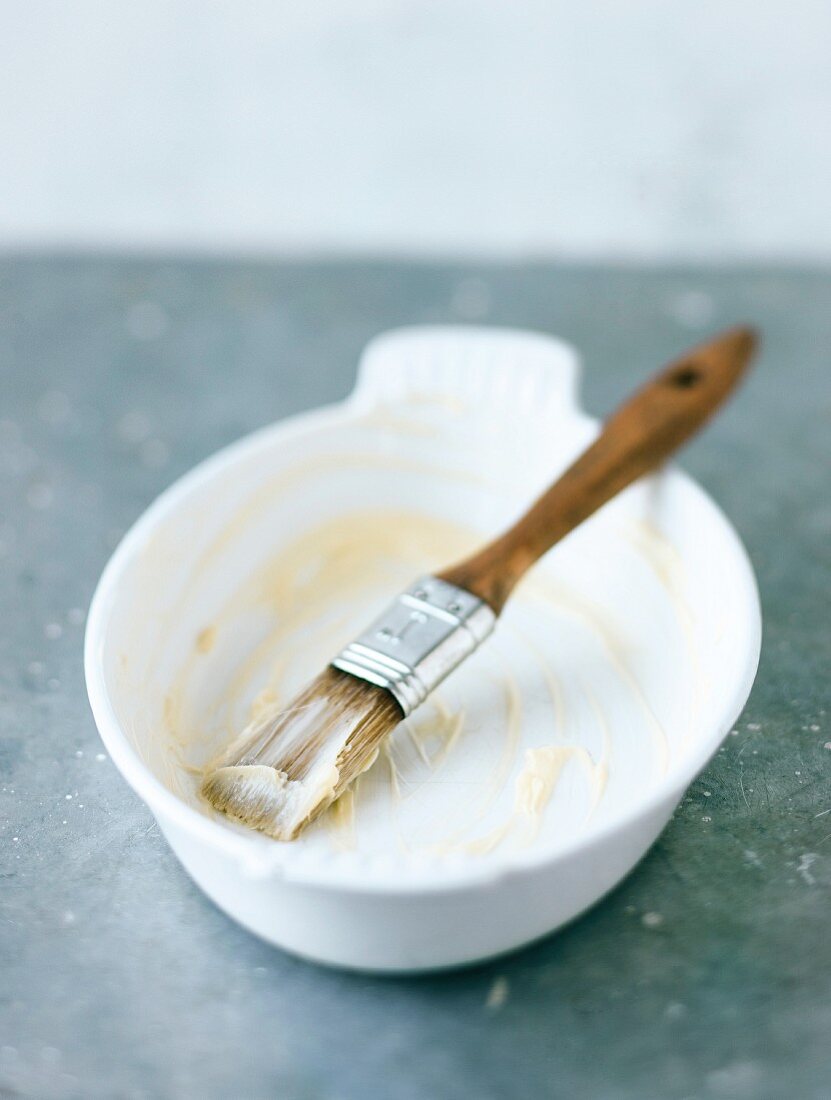 An oven-proof dish being greased with butter