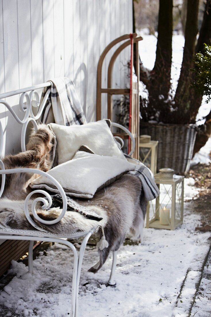 A reindeer fur and cushions on an iron bench in a snowy garden