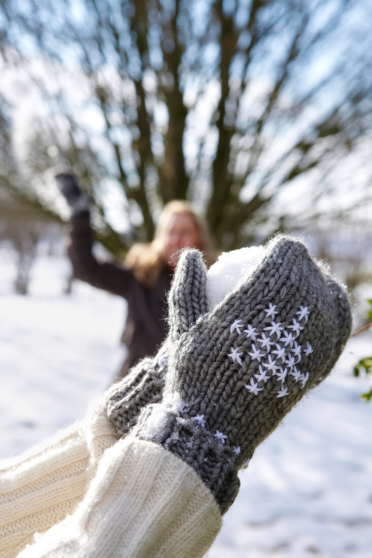 Person wearing woollen gloves with embroidery, making snow balls